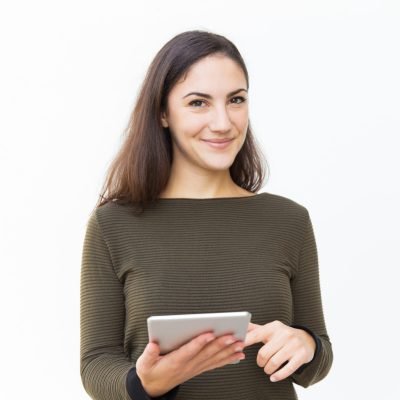 Smiling confident beautiful woman holding tablet, touching screen and looking at camera. Young woman in casual with digital device standing isolated over white background. Communication concept